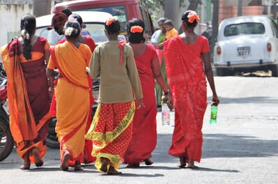 Inde du sud : Plusieurs femmes en saris rouge et orange, s'en vont de dos dans une rue avec une voiture au loin