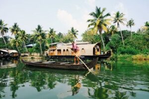 Inde : Sur un canal bordé de cocotiers, un homme essaie de déplacer sa barque avec une longue canne