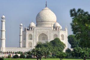 Inde : Le Taj Mahal, mausolée de marbre blanc à dôme sous forme de bulbes, derrière des arbres