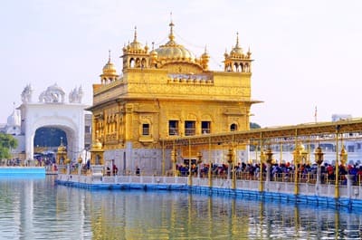 Inde : Une passerelle amène des gens jusqu'à l'entrée d'un temple serti d'or. Le tout est posé sur un lac