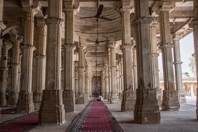 Inde : Une salle avec de nombreuses colonnes et un long tapis au milieu. Un silhouette est assise au loin sur le tapis