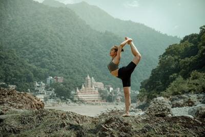 Inde : Une femme pose dans une posture de yoga acrobatique, devant des immeubles et des montagnes verdoyantes