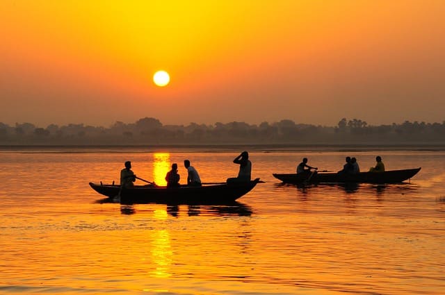 Inde : Des barques avec des silhouette sont sur l'eau, devant un coucher de soleil