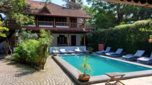 Inde : derrière une belle piscine, une maison avec un balcon en bois, le tout enserré dans un jardin