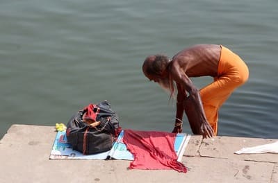 Inde : Un homme en pagne, se baisse au-dessus de l'eau. Ses vêtements sont posés sur la rive