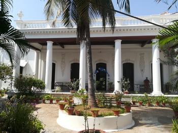 Inde : Un bâtiment colonial avec un perron à grandes colonnes. Il y a des plantations devant
