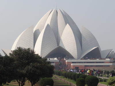 Inde, New Delhi : Un bâtiments avec des pétales blancs en forme de lotus est posé derrière des buissons.