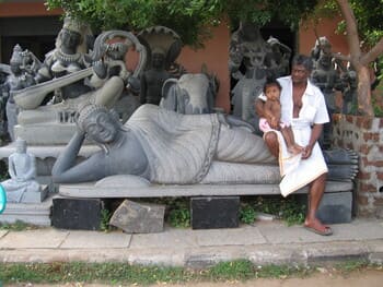 Inde : Un homme tient un bébé sur sa jambe, ils sont assis sur les pieds d'une statue allongée