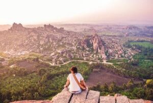 Inde : Une silhouette admire le paysage sur la ville et des rochers, assise par terre les pieds dans le vide