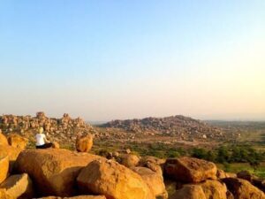 Inde : De gros rochers surplombent une vallée. Un silhouette est assise sur l'un d'eux