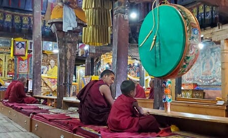 Ladakh : A l'intérieur de la salle de prière d'un monastère bouddhiste, un moine adulte et un enfant sont assis devant un tambour suspendu