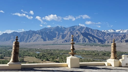 Ladakh : Sur un toit, 3 emblèmes bouddhistes précèdent un paysage verdoyant, cerné de montagnes