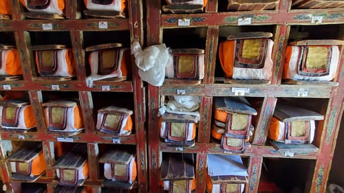 Ladakh : De vieux livres tibétains à l'abri dans des tissus, sont rangés sur des étagères en bois.