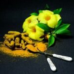 Ayurvéda : Un bouquet de fleurs jaunes est posé sur une table à côté de morceaux de curcuma avec 2 cuillères à café