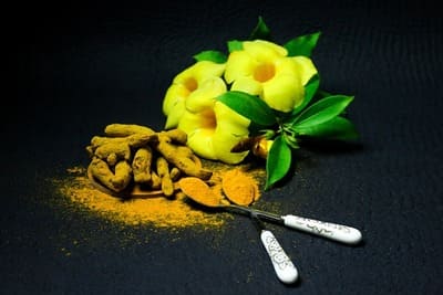 Ayurvéda : Un bouquet de fleurs jaunes est posé sur une table à côté de morceaux de curcuma avec 2 cuillères à café